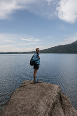 Fototapeta na wymiar Woman Stands on Edge of Large Boulder Along Phelps Lake
