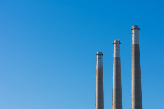 Three towering concrete smokestacks of decommissioned power plant soaring into blue sky.