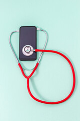Fototapeta na wymiar Top view of red stethoscope with red stethoscope headset listening to cell phone screen on green background. Medical and communications concept or cell phone repair.