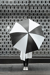 Fashion woman portrait holding umbrella against patterned wall background. White and black color theme conceptual photo. Geometric shapes, unique creative ways 