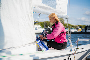 At the yacht parking lot, a young yachtsman in a pink windbreaker prepares her boat for a sailing...