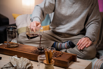 A young man is studying the art of traditional chinese tea ceremony. Brews ripe raw tea in a special glass bowl on a bamboo tray.
