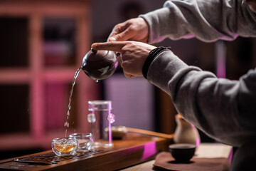 Close-up with the hands of a tea ceremony master in a tea shop, pouring tea for tasting in special cups on a bamboo table with a tray.