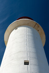 The watch room of a lighthouse.The lantern room has a large green bulb. The building is white with a red rail around the gallery deck.The background is cloudy and there's vignetting around the edges. 