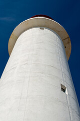 The watch room of a lighthouse.The lantern room has a large green bulb. The building is white with a red rail around the gallery deck.The background is cloudy and there's vignetting around the edges. 