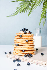 Tall stack of homemade buttermilk pancakes with fresh blueberries on a white wooden board