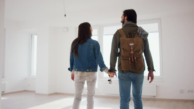 Rear view of young couple with keys moving in new flat, new home and relocation concept.