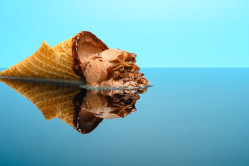 chocolate flavor ice cream cone in a melting process on glass with reflection on blue background