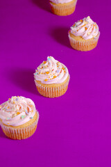 Pink frosted vanilla cupcakes with sprinkles on a bright purple background