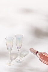 Сlosed bottle of rose champagne sparkling wine and glasses with sunlight on light table