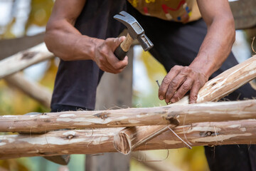 Close-up of a man hammering nails on a eucalyptus wood roof frame. House design using miniature eucalyptus