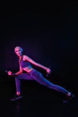 Fototapeta premium A slim, fit girl is stretching on a black background in a mixed color light. Self-improvement and fitness exercises for women. Copy space neon trend