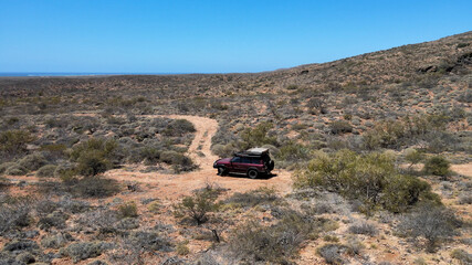 Aerial shot of 4x4 safari vehicle driving on hilly desert during sunlight. Exmouth, Western Australia.