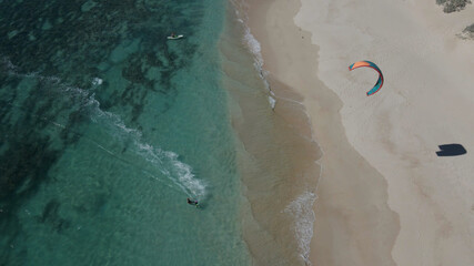 Aerial overhead shot showing kite surfer surfing on clear Pacific Ocean during beautiful weather outside.