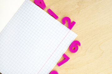 On the wooden table is an open notebook with a checkered sheet and pink plastic numbers. Educational concept