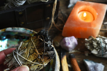 A close up image of a burning white sage smudge stick with selenite candle.