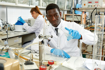 Serious male scientists with glass test tubes during chemical experiment , woman on background