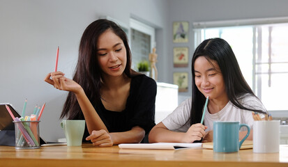 Asian mother helping her daughter doing homework with digital tablet at home.