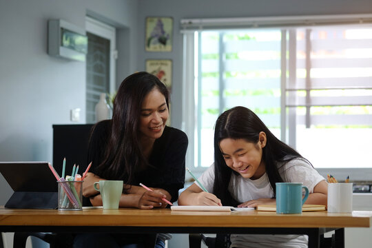 Asian mother helping her daughter doing homework with digital tablet at home.