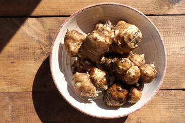 Jerusalem artichoke roots in a bowl on wooden table. Top view of fresh raw topinambour potato on rustic background
