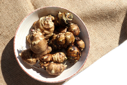 Jerusalem artichoke roots in a bowl on burlap texture. Top view of fresh raw topinambour potato on rustic background