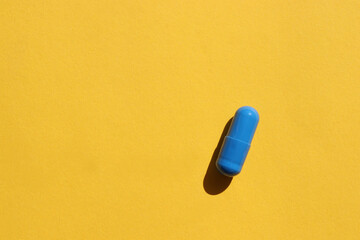 Single blue pill on a yellow paper background. Top view, copy space. Hard light, shadow. Medicine capsule on colored backdrop