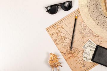 world map, straw hat, black leather wallet with money, sunglasses, pencil and shell on a white wooden table