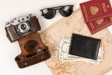 world map, two passports, money in a black leather wallet, an old film camera in a leather case and sunglasses on a table. view from above. selective focus. inscription - passport Russian Federation