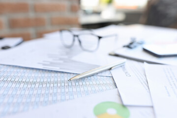 Ballpoint pen and glasses lying on documents with numbers closeup