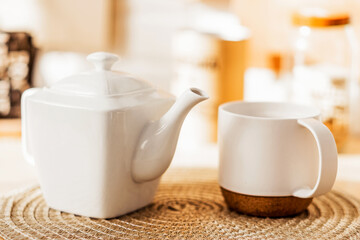 White cup and teapot stand on the table on a wicker napkin