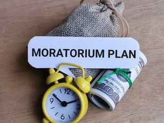 Economy and finance concept. Phrase MORATORIUM PLAN written on bubble speech with sack of money,alarm clock and fake money.