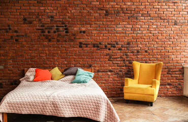 Modern double bed and yellow armchair stand against brick wall background