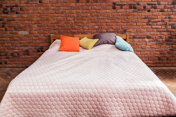 Modern double bed with a plaid and colorful pillows stands against a brick wall background