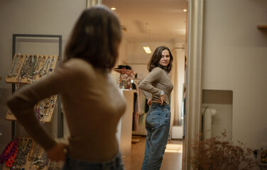 Beautiful young woman standing in front of a mirror in a clothing boutique trying on a new look