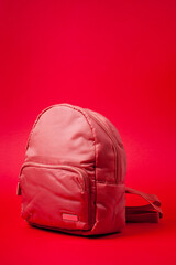 Naklejka premium Children's backpack in pink fabric with shoulder straps, shot against a rich red background.