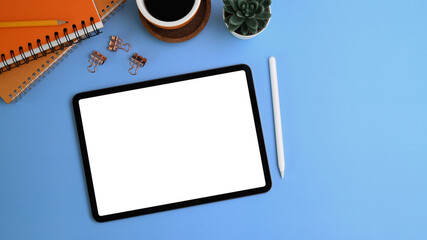 Mock up digital tablet, stylus pen, succulent plants, coffee cup and notebook on blue background.