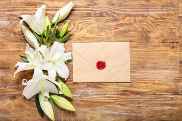 Beautiful lily flowers and envelope on wooden background