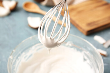 Bowl with coconut cream and whisk on color background, closeup