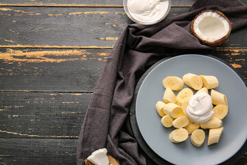 Plate with cut banana and coconut cream on dark wooden background