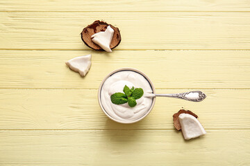 Bowl and spoon with coconut cream on color wooden background