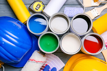 Cans of paints and tools on color wooden background