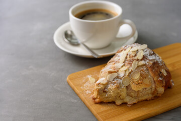 Almond croissant on wooden board with black coffee on concrete grey background