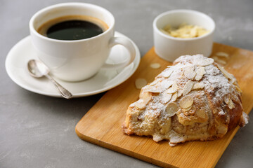 Almond croissant on wooden board with black coffee on concrete grey background