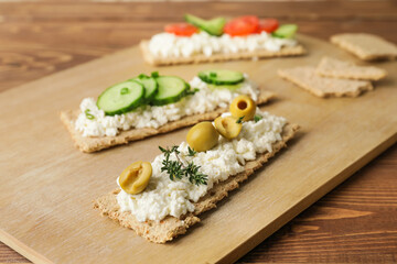 Crispbreads with cottage cheese and vegetables on wooden background