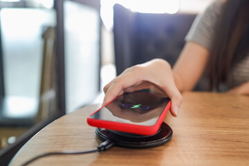 Charging mobile phone battery with wireless device in the table. Smartphone charging on a charging pad. Mobile phone near wireless charger.