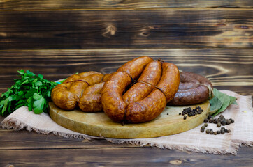 A set of traditional homemade smoked and raw sausages on a round wooden board. Dark wooden rustic background. Copy space