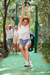Obraz premium Group of happy men and women rolling on zipline one by one at adventure park