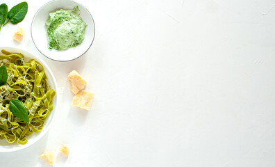 Green noodles with spinach and parmesan cheese in a white plate on a white table. Basic ingredients. Healthy food. View from above. Copy space