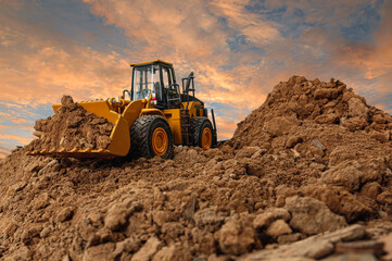 Fototapeta Wheel loader are digging the soil in the construction site on the  sky background after sunset obraz