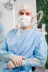 Portrait of young male dentist wearing disposable clothes sitting in modern clinic